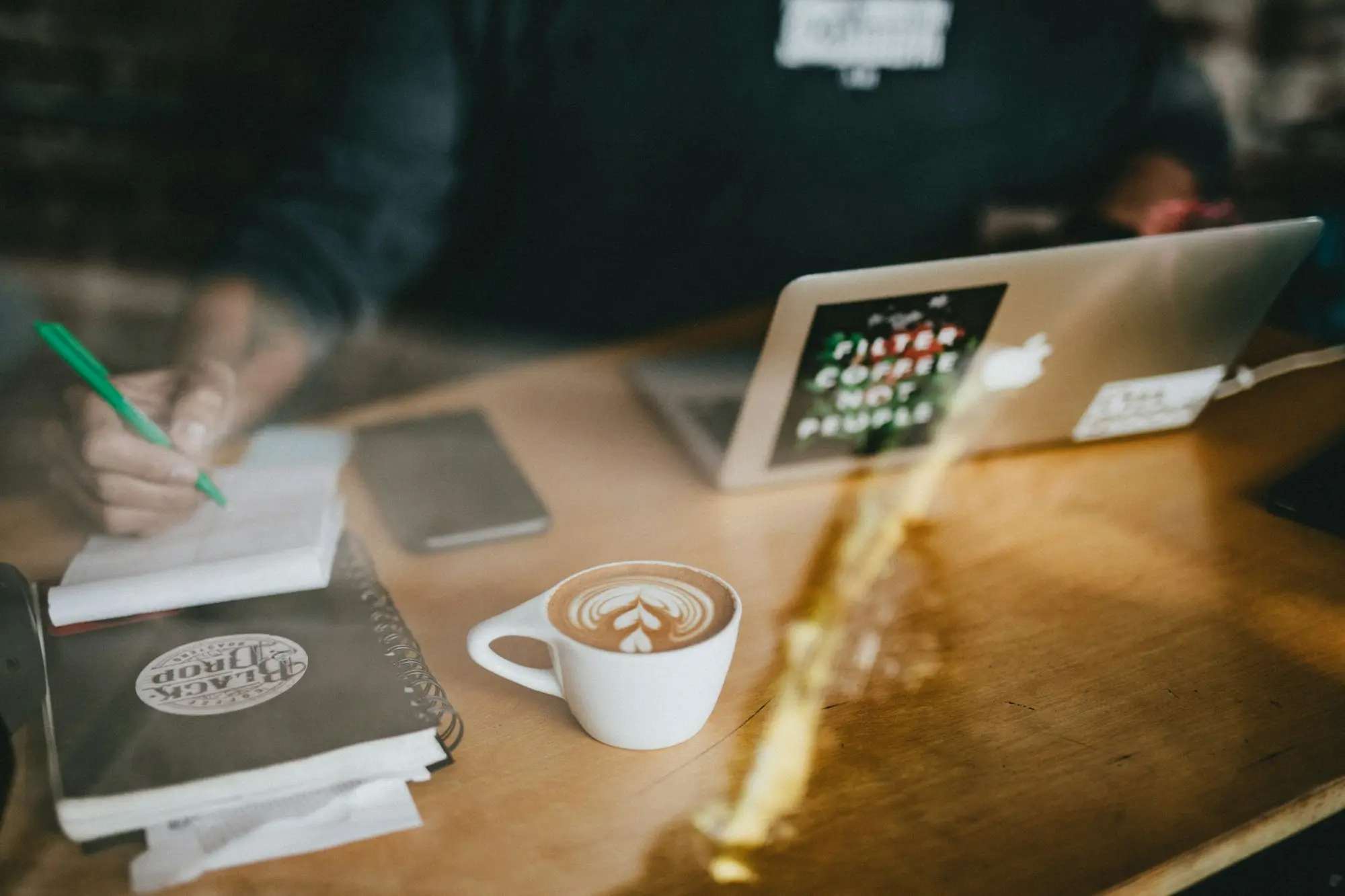 Writing a plan in a notebook beside a coffee at a café table